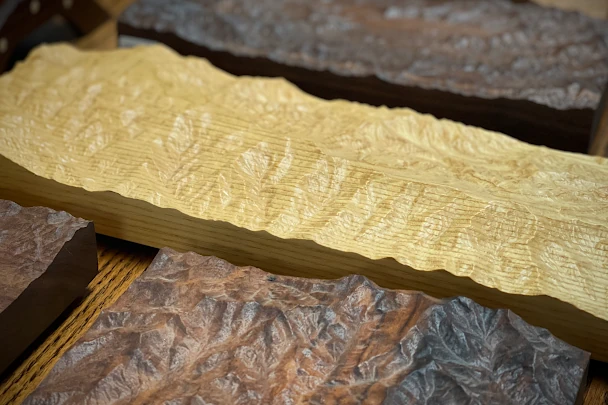 Golden ash wood carving of a mountain ridgeline, elongated piece on a workbench